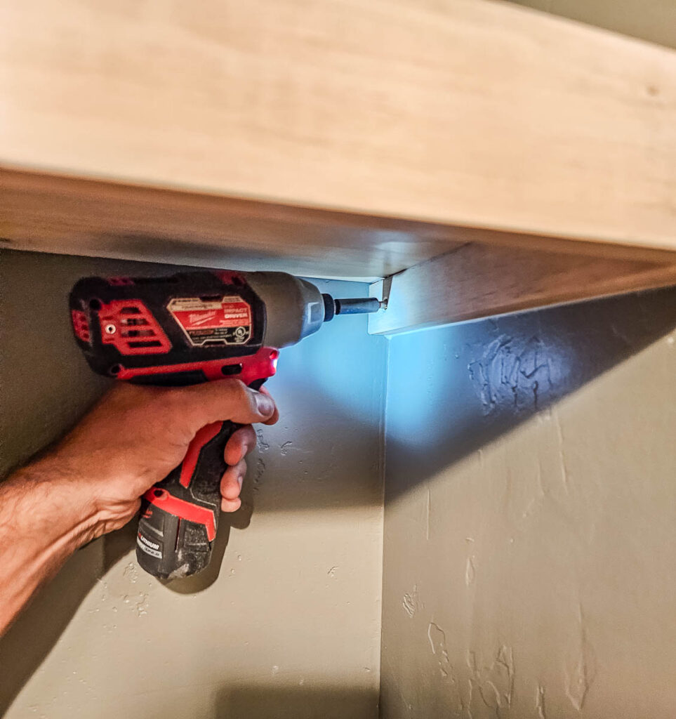 A man is using a tool to attach the floating bookshelves.