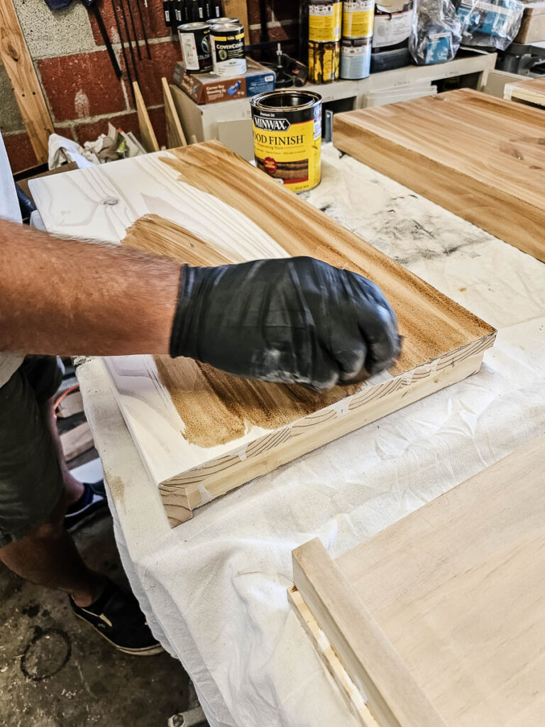 Then, a man is applying a neutral wood tone stain to the floating bookshelves.