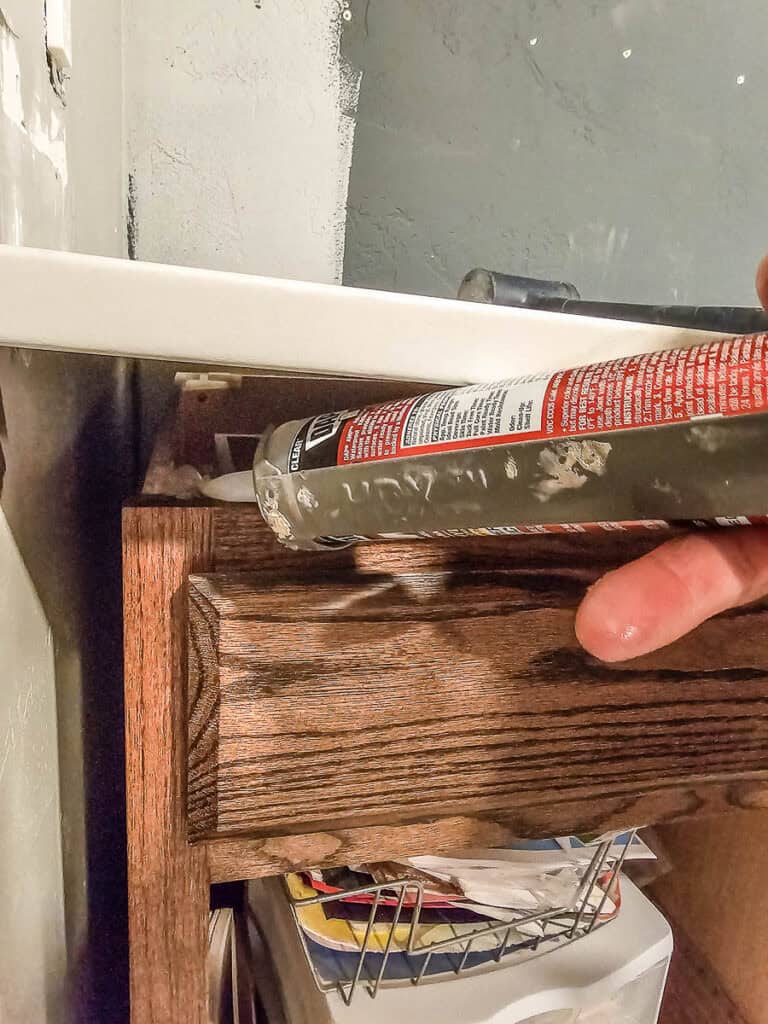 A photo of silicone applied on top of the cabinets with a caulking gun to secure the countertop, allowing it to dry before continuing