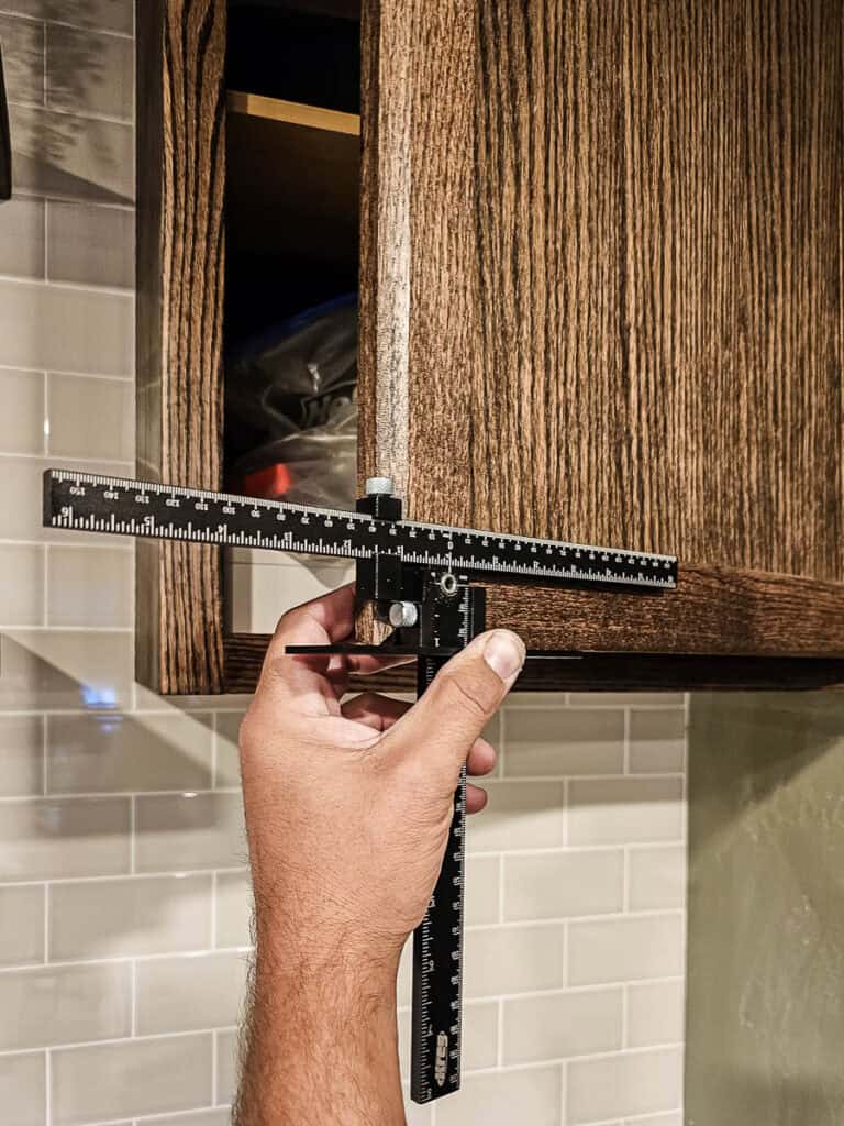 A photo of hardware being installed on DIY built-in cabinets made from stock cabinetry in a dining room.