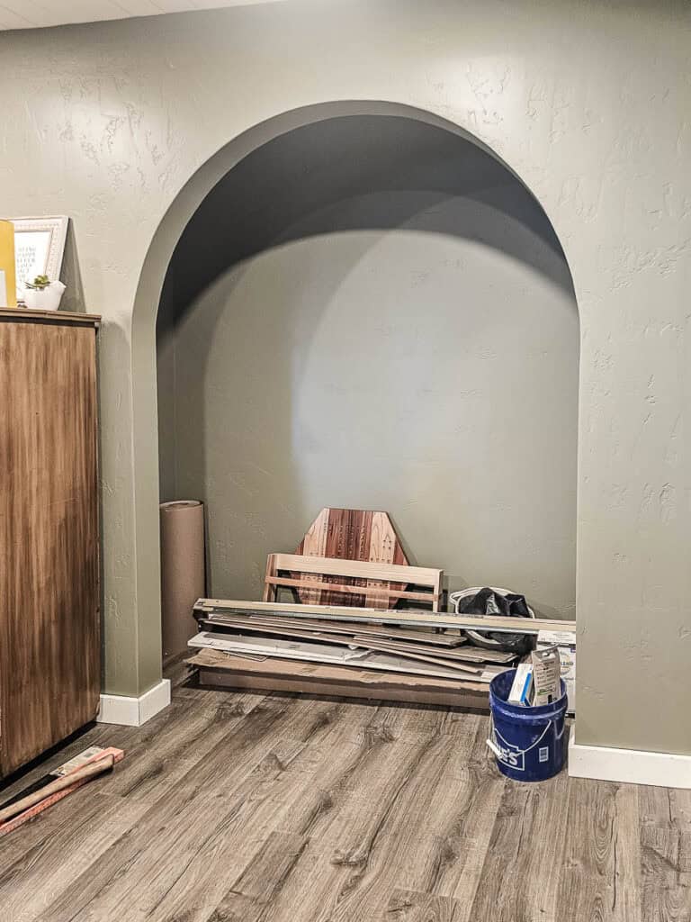 Closet with doors removed and archway opening with pile of things laying on the floor before it was converted into a reading nook for kids