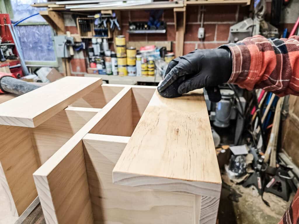 A photo of a man applying a stain to the small bookshelf, using a brush to evenly coat the wood, followed by sealing it to give the finished piece a smooth and polished look.