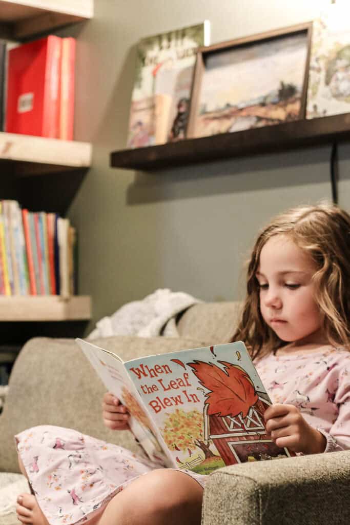 Girl sitting in reading nook in old closet reading a picture book with book shelves in the background