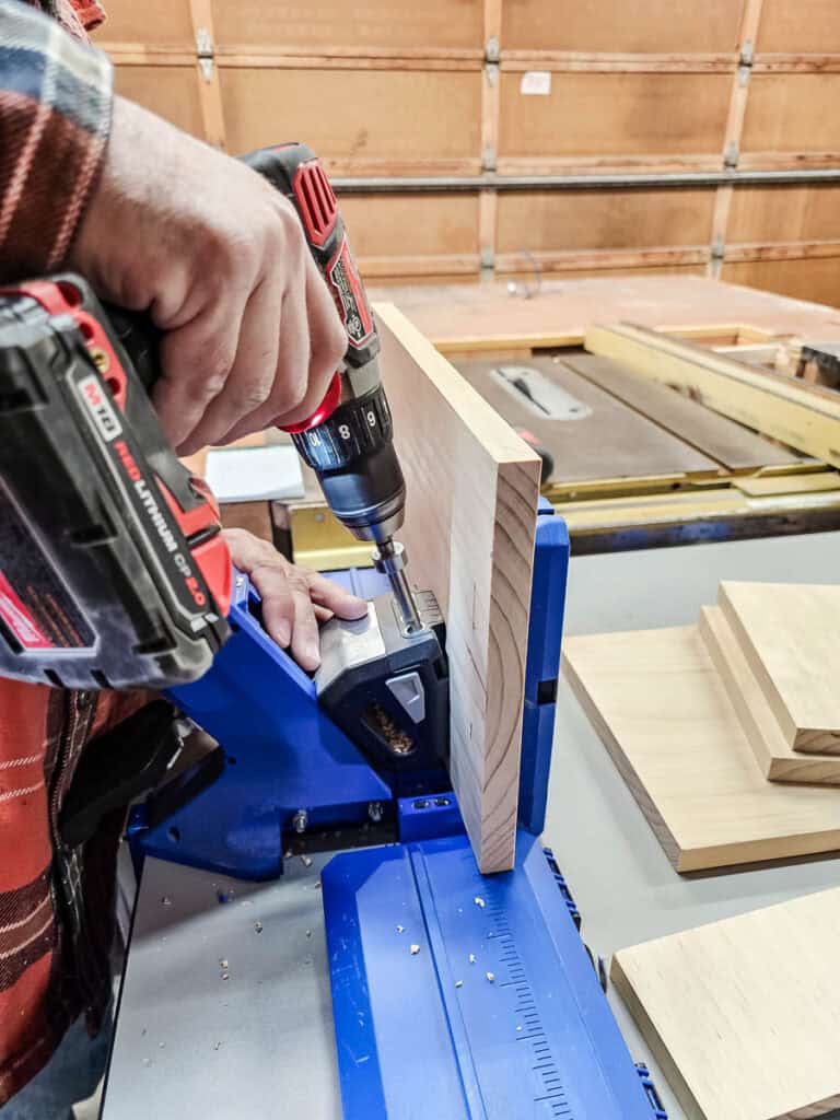 A photo of a man drilling into a wooden board as part of the process to create a small bookshelf from a single piece of wood.