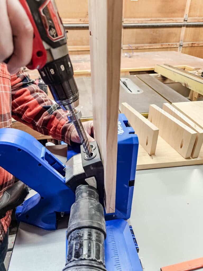 A photo of a man using a custom plug cutter to drill into a wooden board, preparing to insert wooden plugs for a clean, professional finish while assembling a small bookshelf.