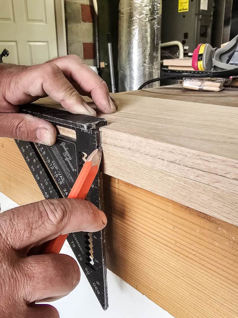 Marking oak wood with speed square before joining together with dowel joinery to make U-shaped faux wood beams for cased openings in open concept