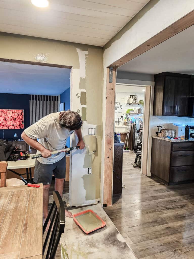 A photo of a man painting the wall sage green using a roller, as part of a transitional dining room makeover.







