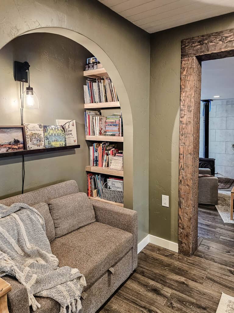 Reading nook in dining room and homeschool room with sage green walls with small couch and bookshelves 