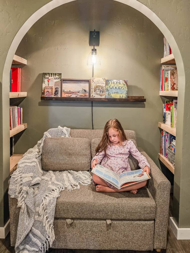A girl reading a book on a small sofa in a traditional-style dining room.