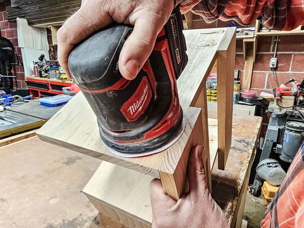 A photo of a man sanding, staining, and sealing a small bookshelf, carefully applying the finishing touches to the wood to enhance its appearance and durability.