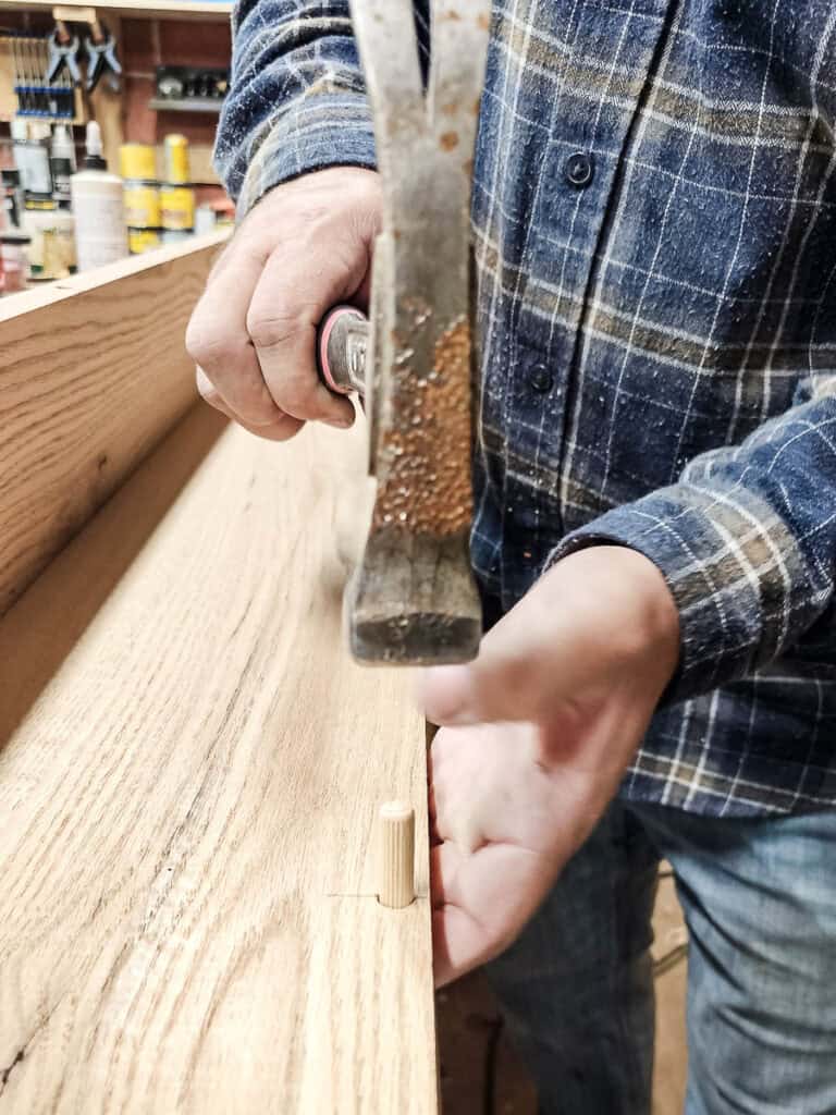 Tapping dowel into place in hole with hammer for dowel joinery with wood