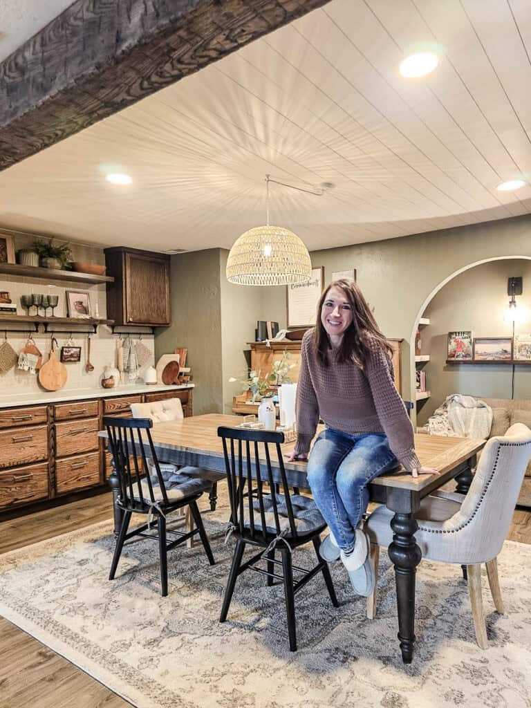 Woman sitting on rectangular shaped dining room table with black turned legs and extendable leaf to make the table bigger