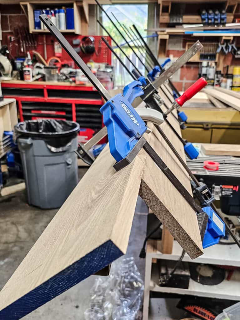 Two pieces of wood glued together and clamped after being joined with dowel joinery to make fake wood beams