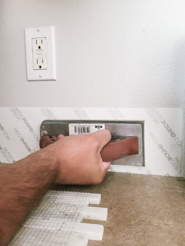 A person applying the Musselbound Adhesive Tile Mat to the walls.