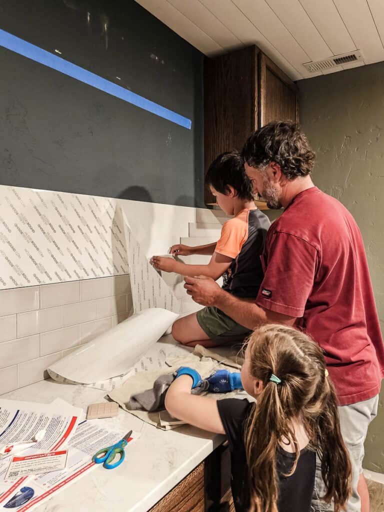 A man and children enjoying the process of applying the Musselbound Adhesive Tile Mat to the walls