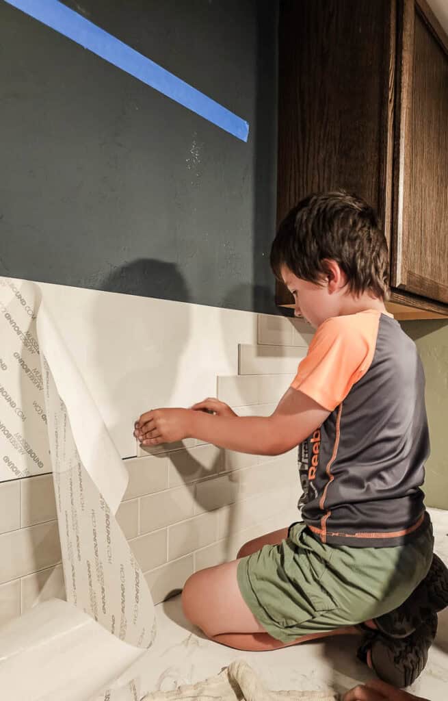 A boy helping to apply an adhesive tile mat.