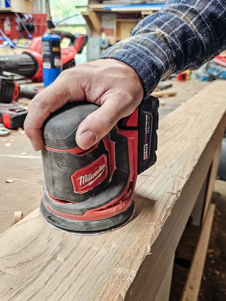 A photo of a man sanding the wood to smooth its surface.