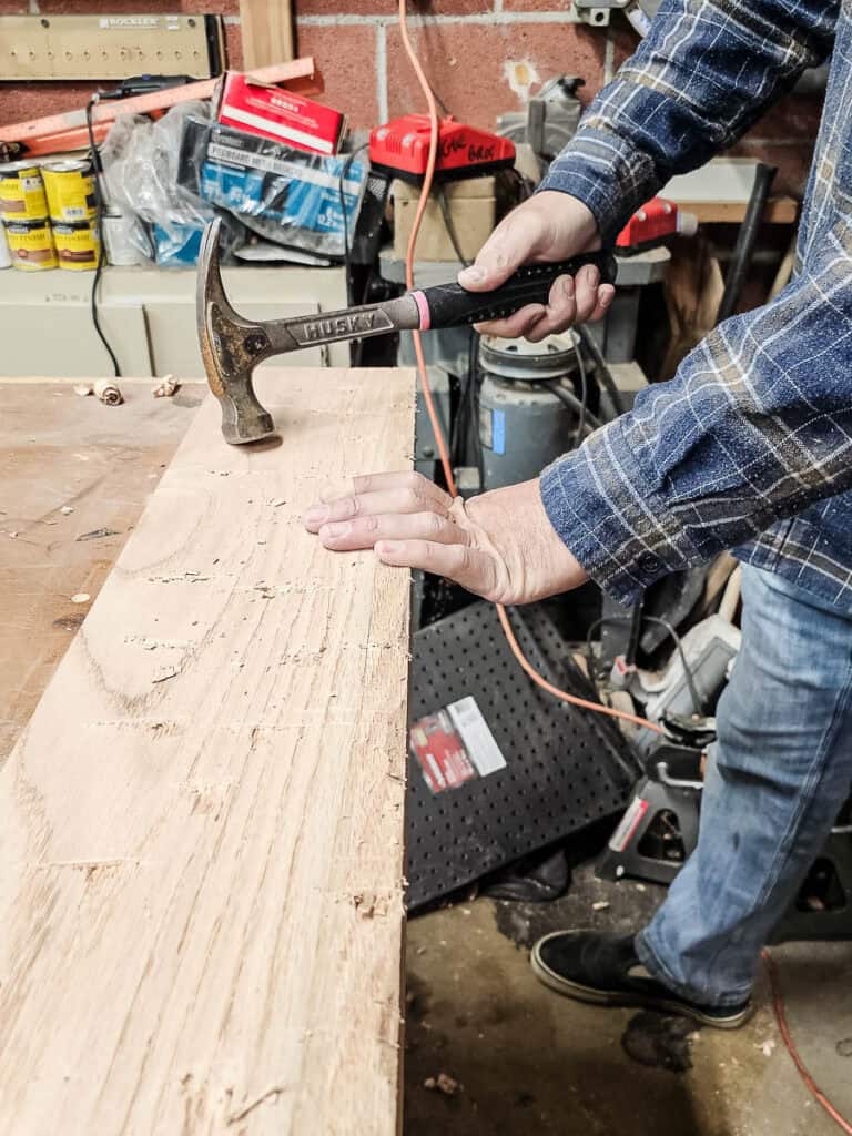A photo of a man denting wood with a hammer.