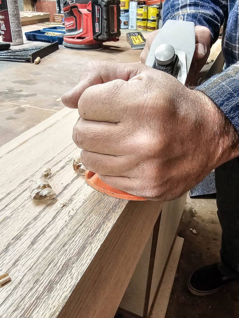 A photo of a man using a sharp blade to plane wood and smooth its surface.