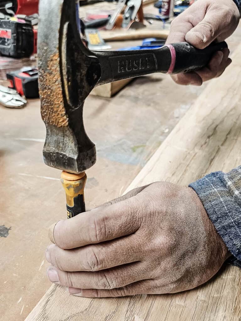 A photo of a man using a nail punch to create holes in the wood.