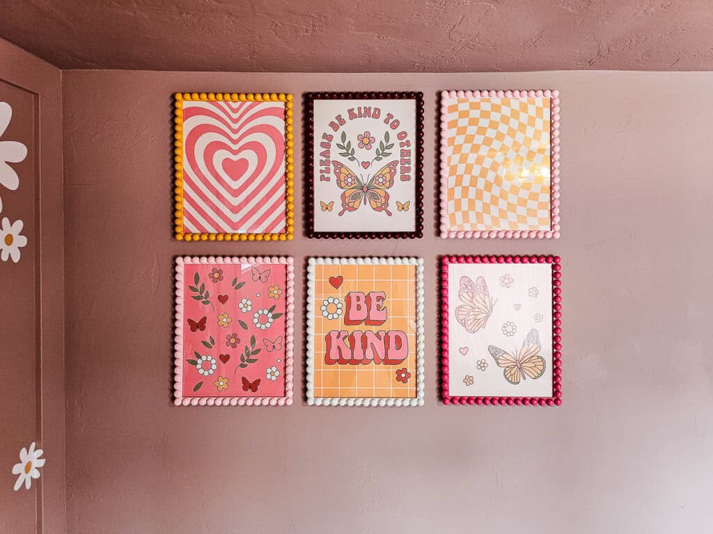 A photo of six finished wooden bobbin picture frames hanging on the wall, each painted in a different color.