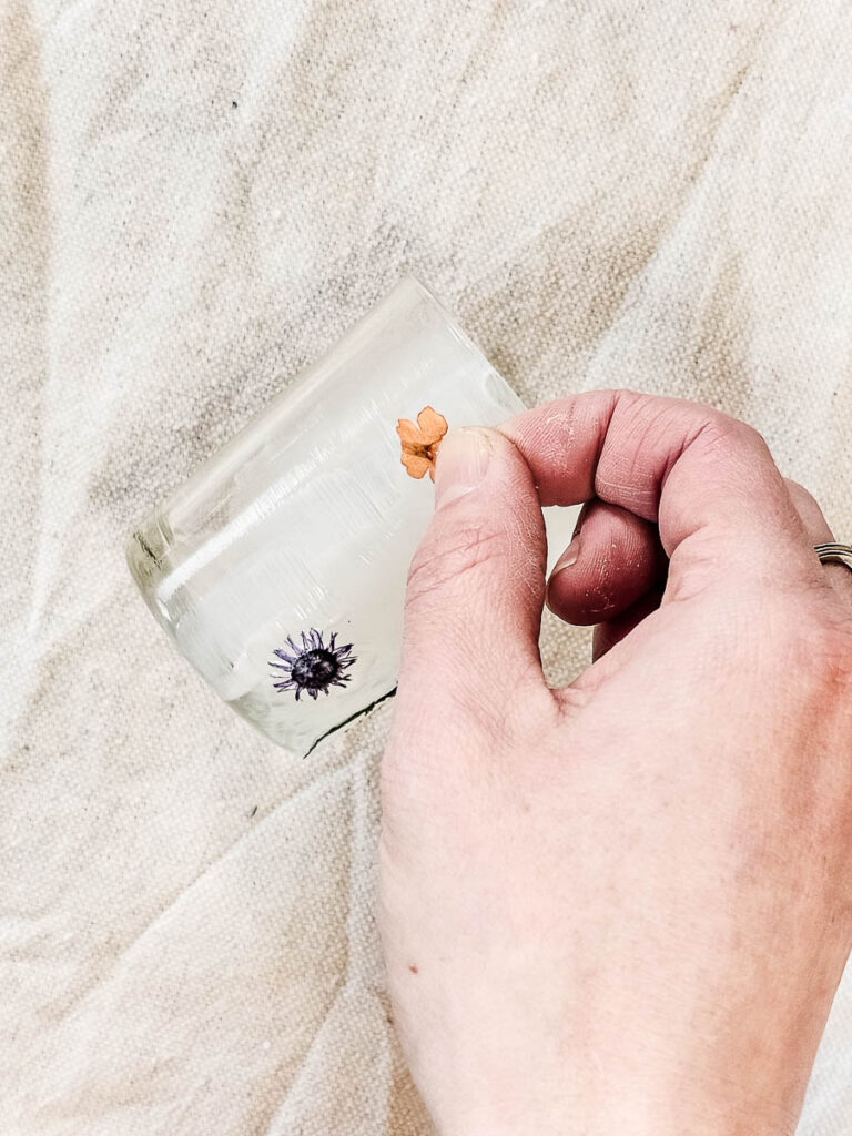 A person pressing a flower while painting the glass with a brush.
