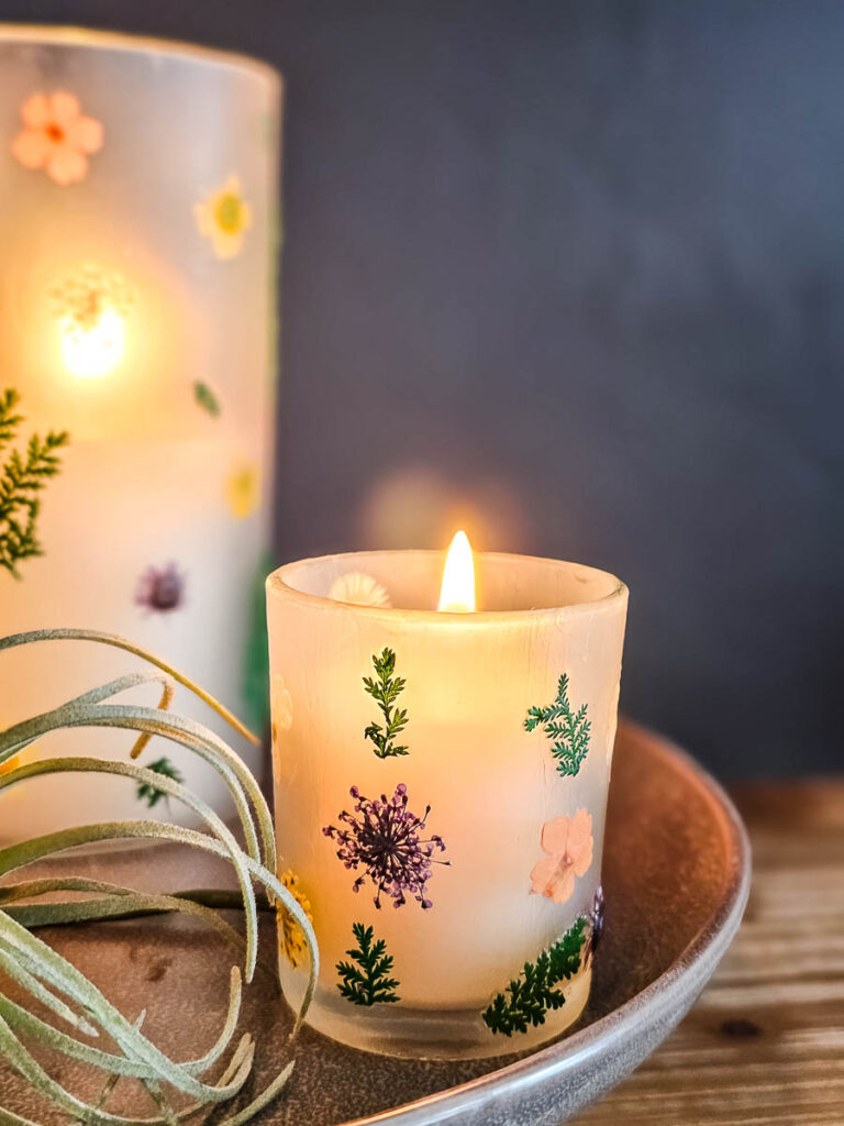 A close-up photo of a glass candle holder featuring delicate hand-painted floral designs.
