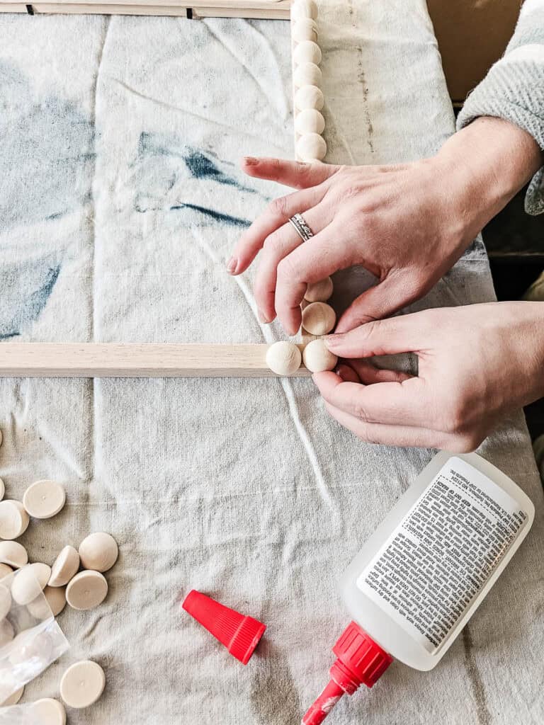 A woman gluing wooden beads onto the frame.