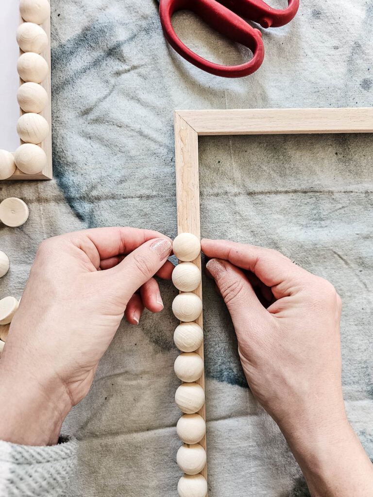 A photo of a woman attaching wooden beads along the edges of the frame.

