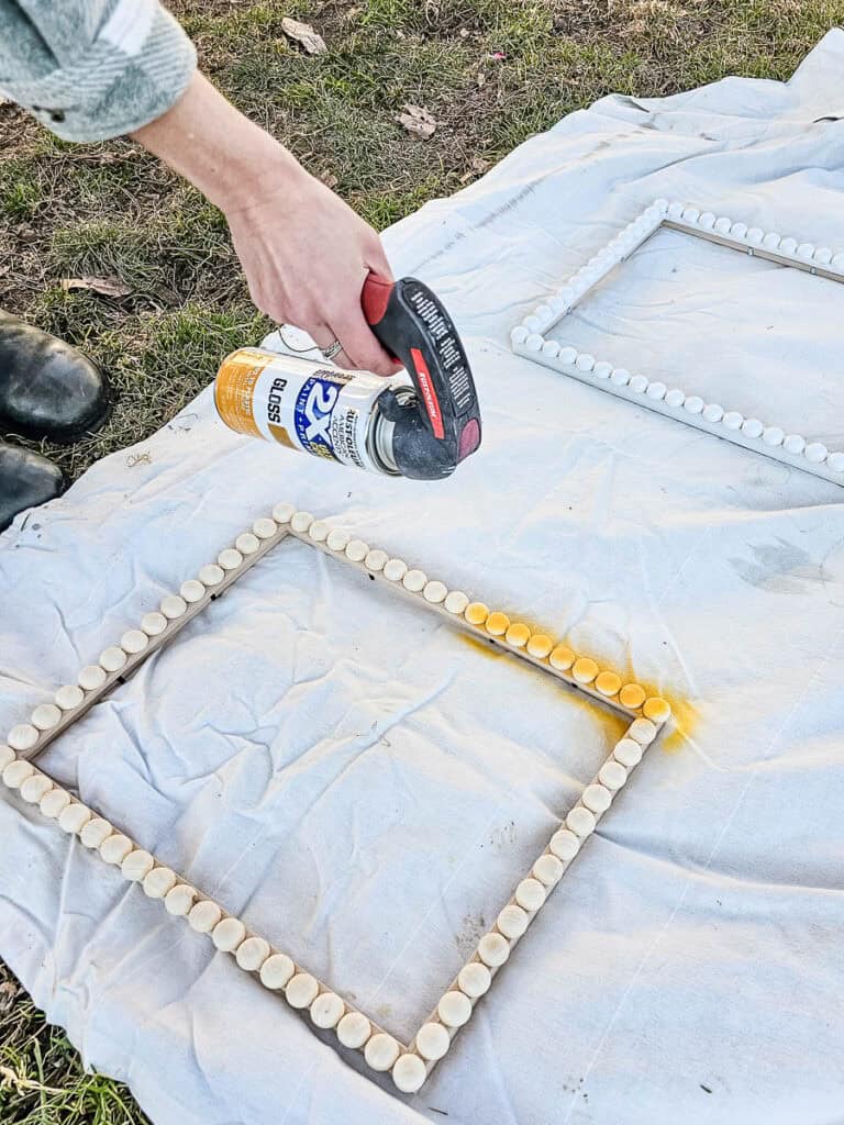A photo of a woman spraying the frame with acrylic paint.

