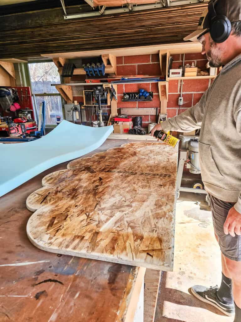 Continue spraying the cloud-shaped wooden figure with multi-purpose spray adhesive before attaching foam
