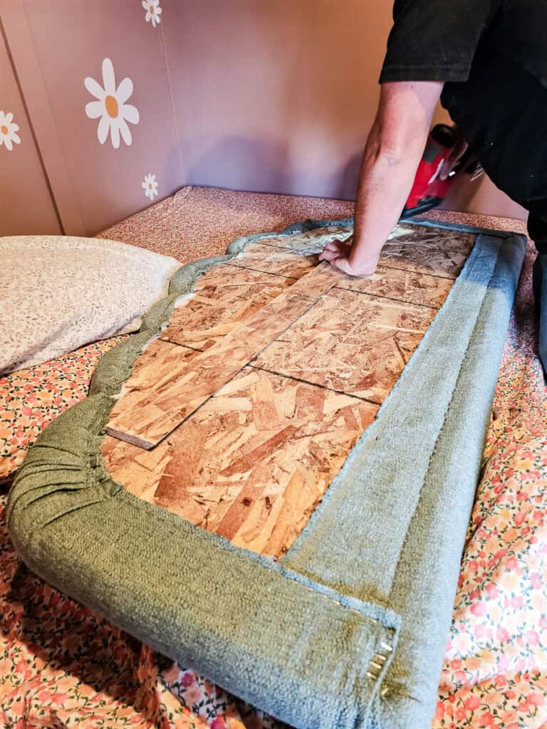 A man is using a brad nail gun to secure one side of the French cleat made with scrap wood to the cloud-shaped headboard.