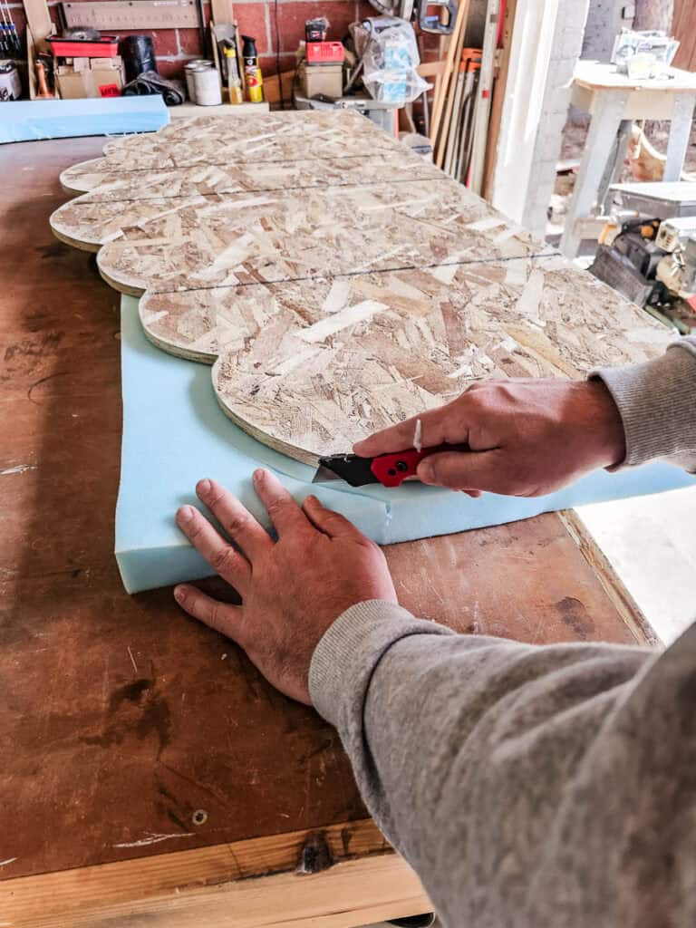The man is continue cutting the cloud shaped foam for the headboard with a utility knife 