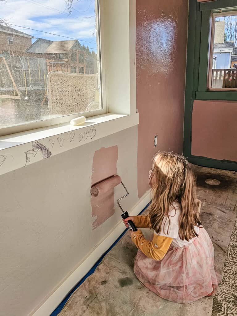 A little girl painting the wall pink.