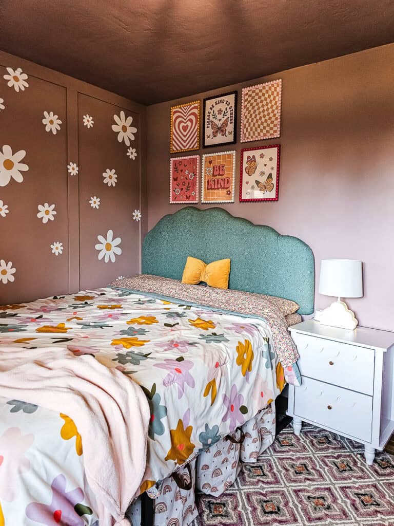 Turquoise upholstered cloud headboard hanging on the wall behind a bed in little girl's bedroom with floral bedding and pink walls with a white scallop nightstand and cloud table lamp
