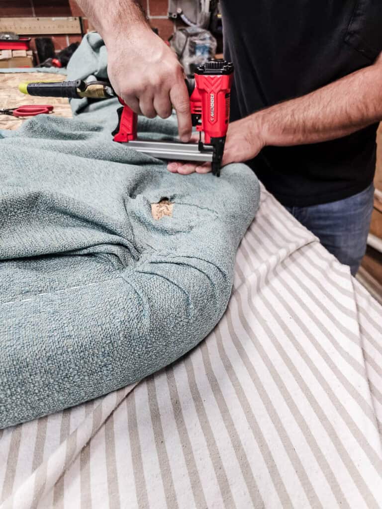 A man is stapling fabric over the cloud-shaped headboard with folding on the corners where necessary 
