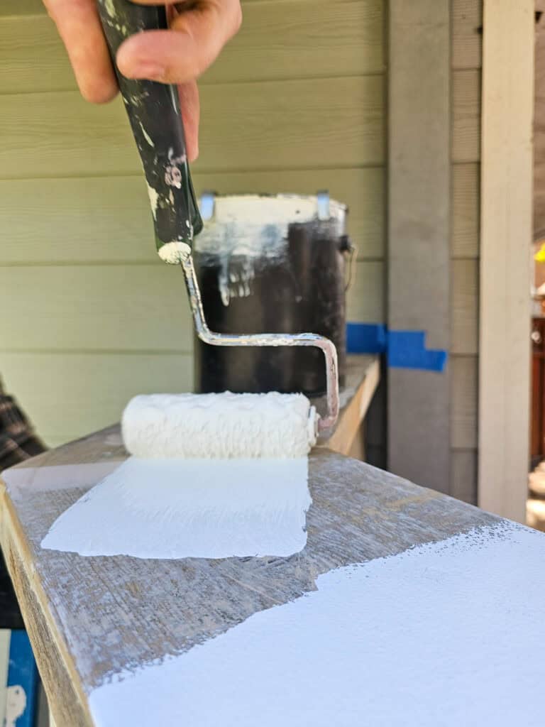 Photo of a person using a paint roller to apply paint to wood.