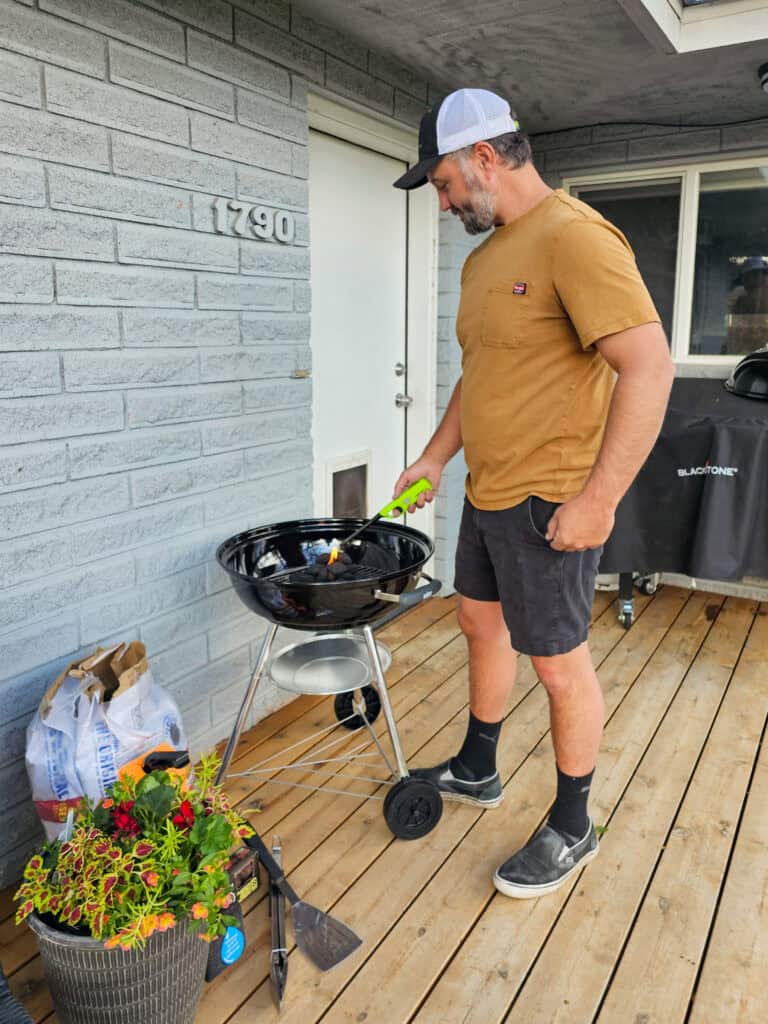 A photo of a man grilling with a black charcoal grill in the backyard.