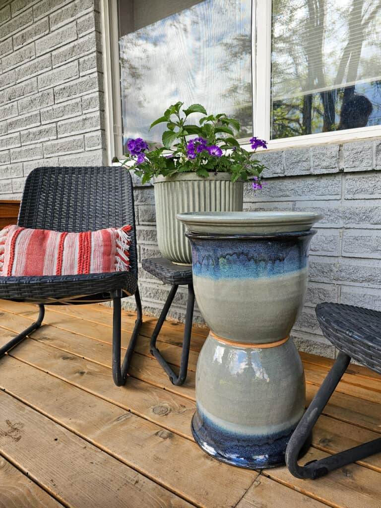 Close-up photo of a patio side table placed between two outdoor chairs, highlighting the table's surface and details.
