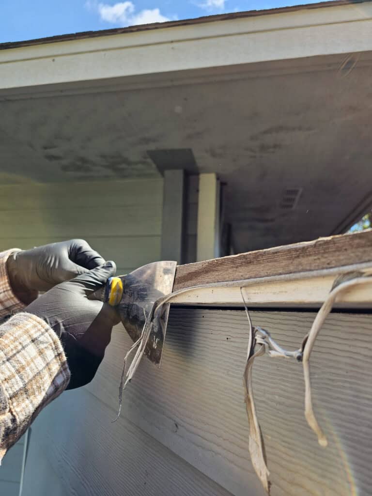 A photo of a man removing loose, damaged wood material during a repair project.
