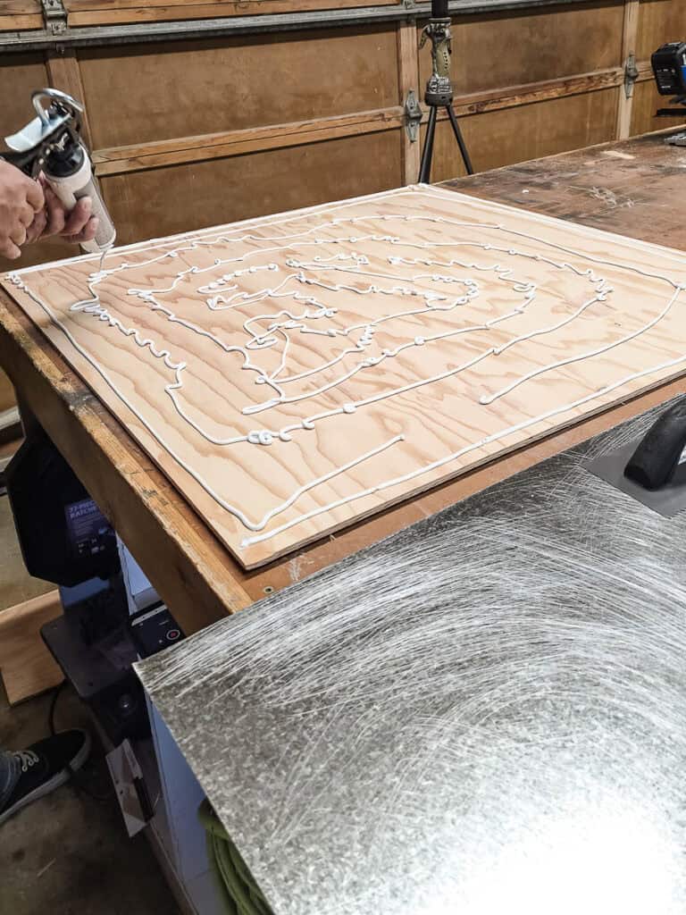A second image showing the man applying construction adhesive to the 3x3 plywood board.