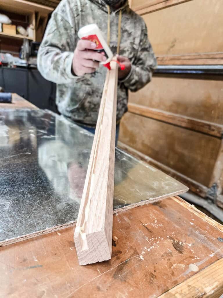 A man applying wood glue along the inside grooves of the frame pieces before sliding them over the plywood and metal edges.