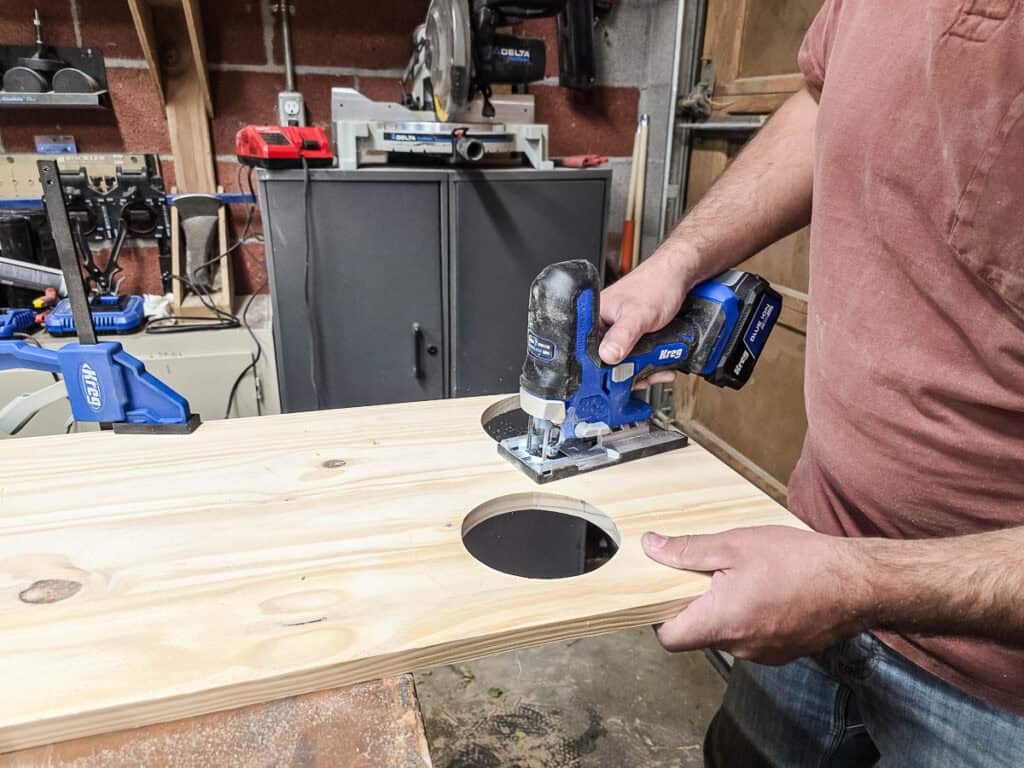 A man using a jigsaw to cut out O's on a project panel for the Tic Tac Toe board.