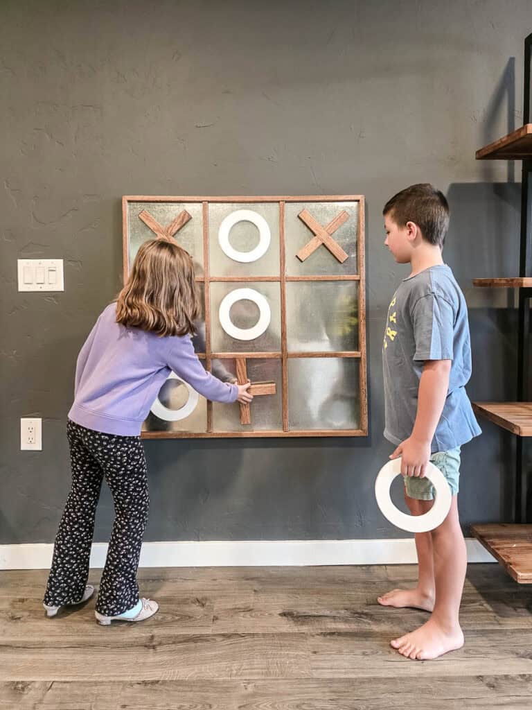 Two kids playing with the finished giant DIY Tic Tac Toe board on the wall