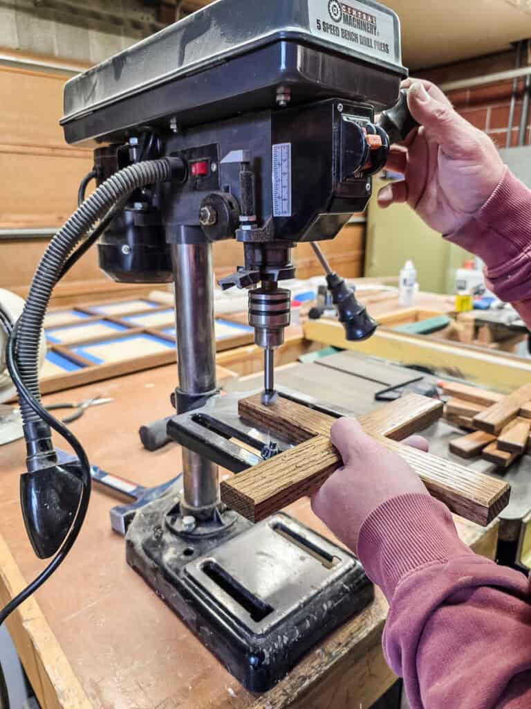 A man drilling a shallow hole in the wood with a drill press to insert a magnet.