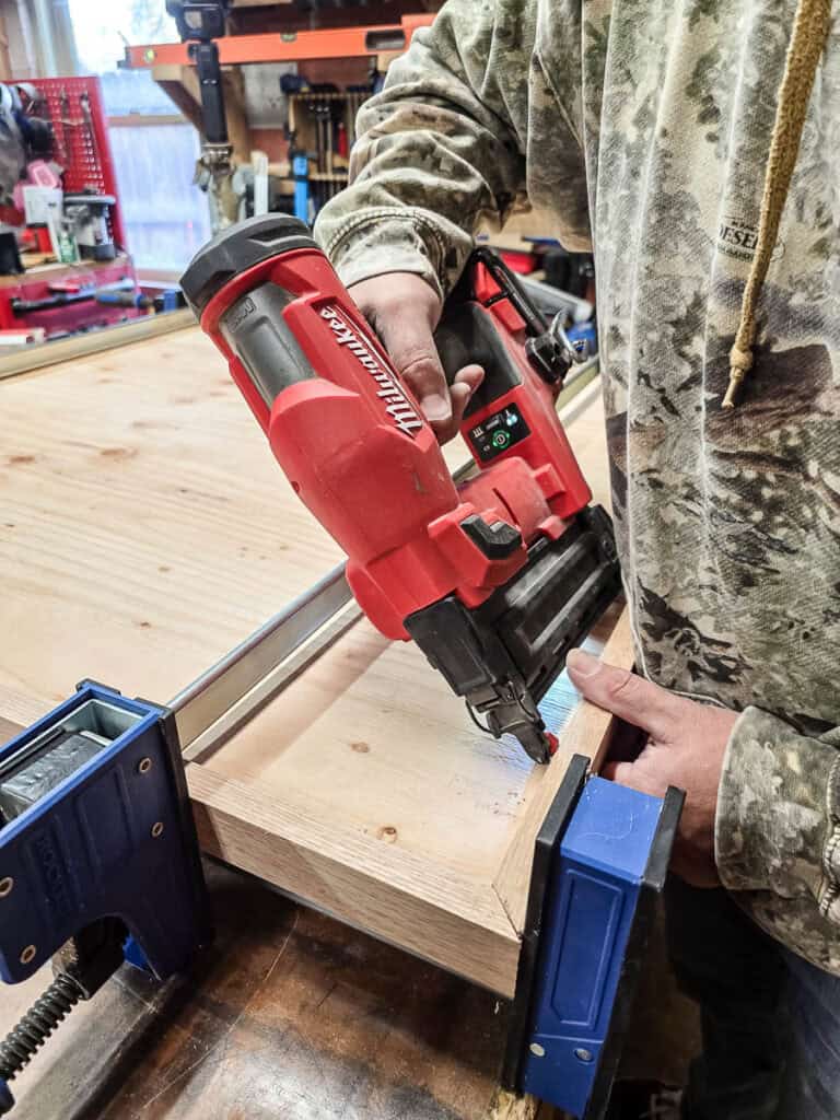 A photo showing a man using clamps and nails to fasten the frame from the back.