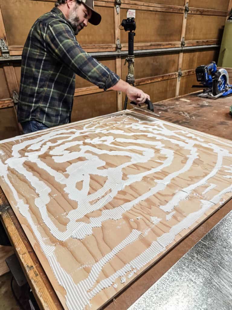 Man tooling construction adhesive on sheet of plywood with trowel