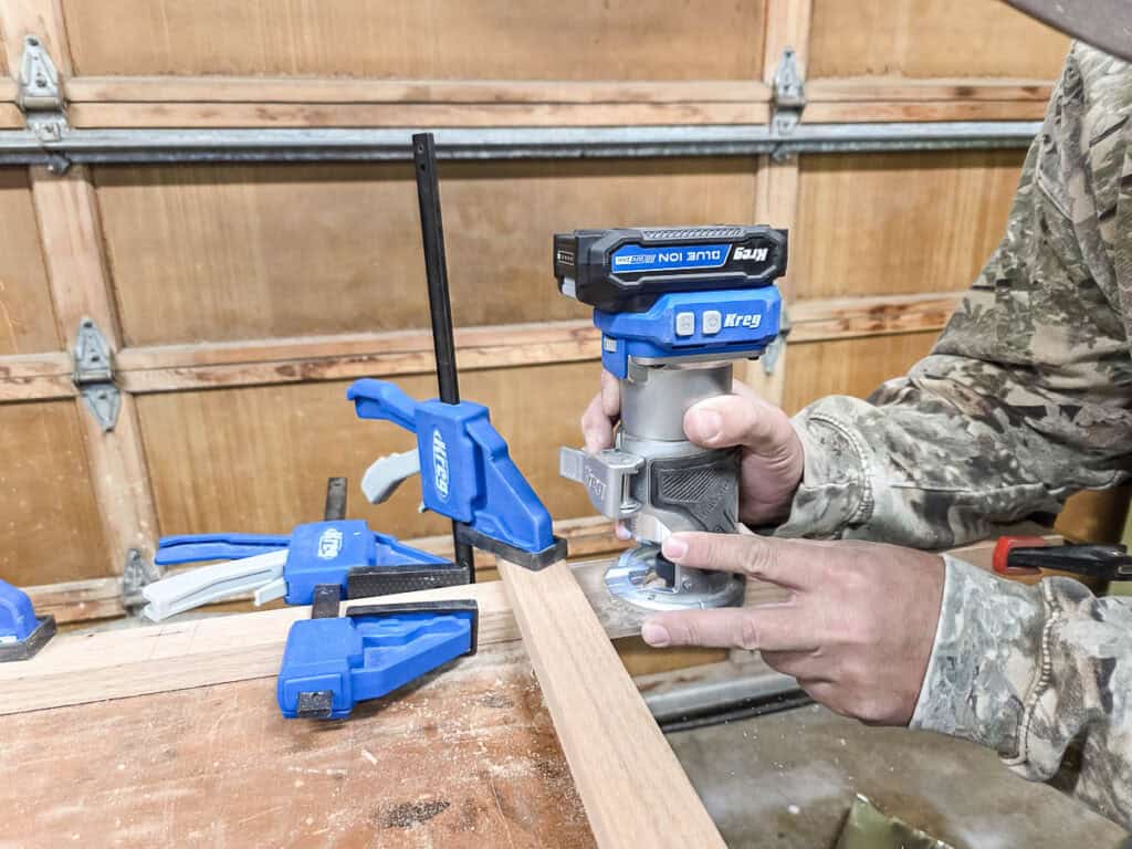 A man cutting grooves for the grid pieces with a trim router to form the Tic Tac Toe board.