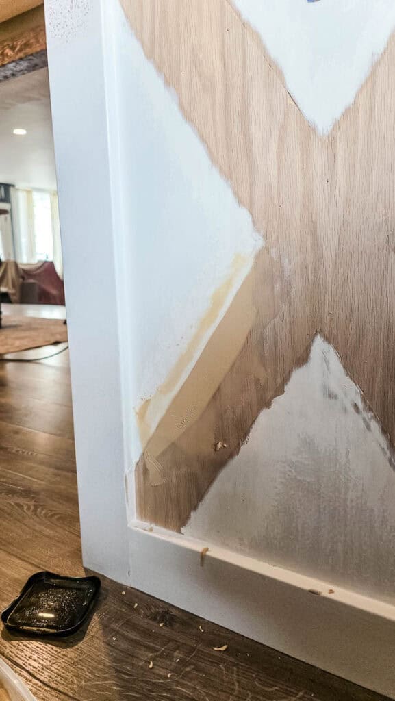 Close-up of a kitchen island with decorative X-pattern trim being repaired with wood filler after sanding, preparing the surface for priming and painting.
