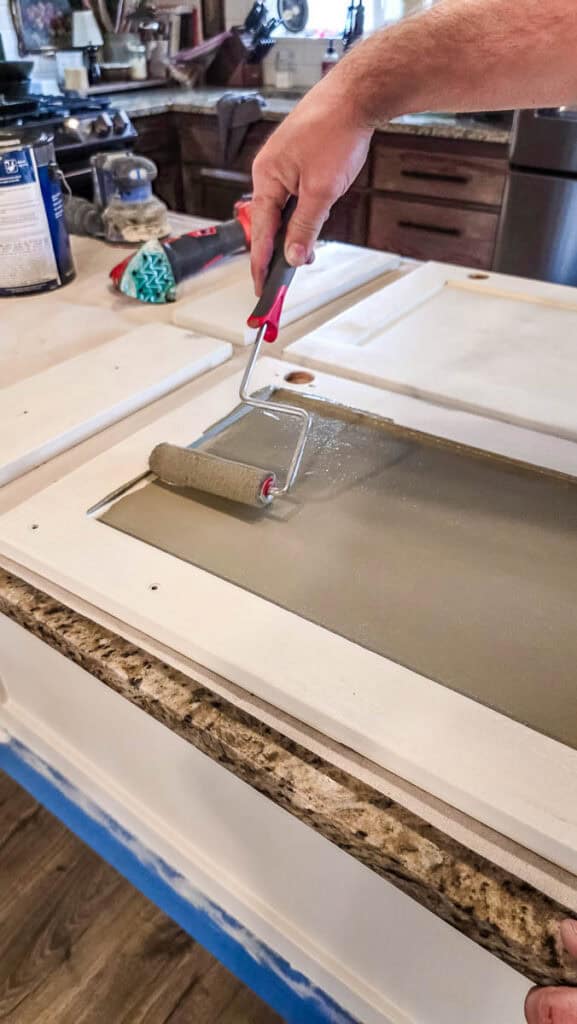Foam roller applying cabinet paint to a detached kitchen cabinet door during a kitchen island painting project for a smooth, even finish.